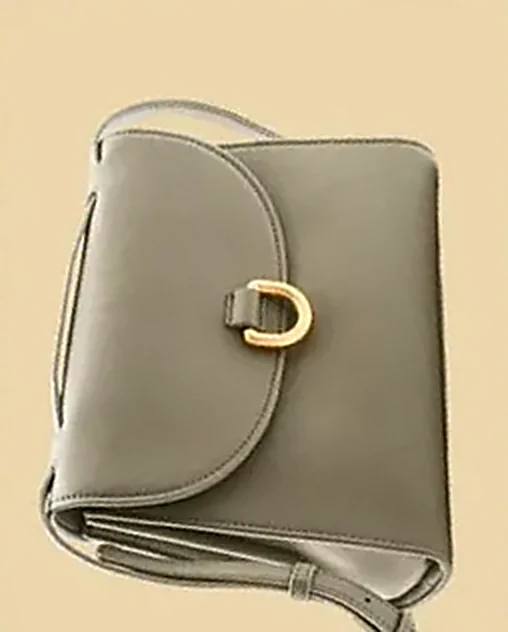 Olive leather shoulder bag with a gold horseshoe clasp on a soft sand backdrop